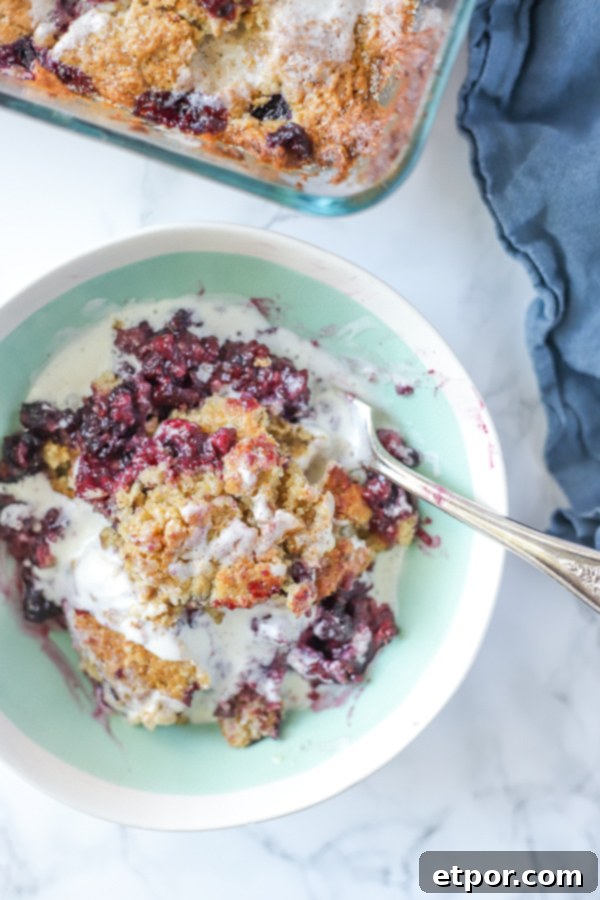 Blackberry cobbler fresh out of the oven, drizzled with cream, with a wooden spoon ready to scoop. A perfect homemade dessert.