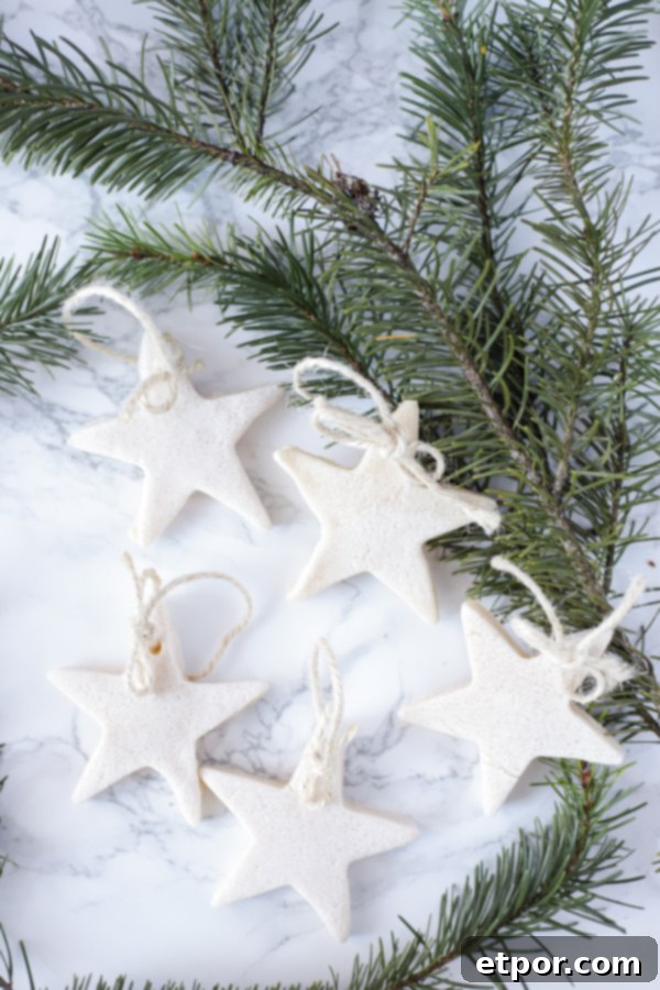 5 salt dough ornaments with twine on a marble countertop with fresh greenery behind