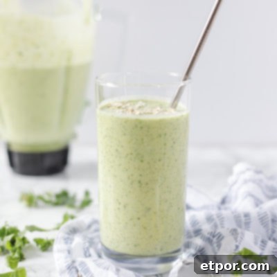 Glass of a tropical green oatmeal smoothie on a blue and white napkin with a blender jar in the background with remaining smoothie in it.
