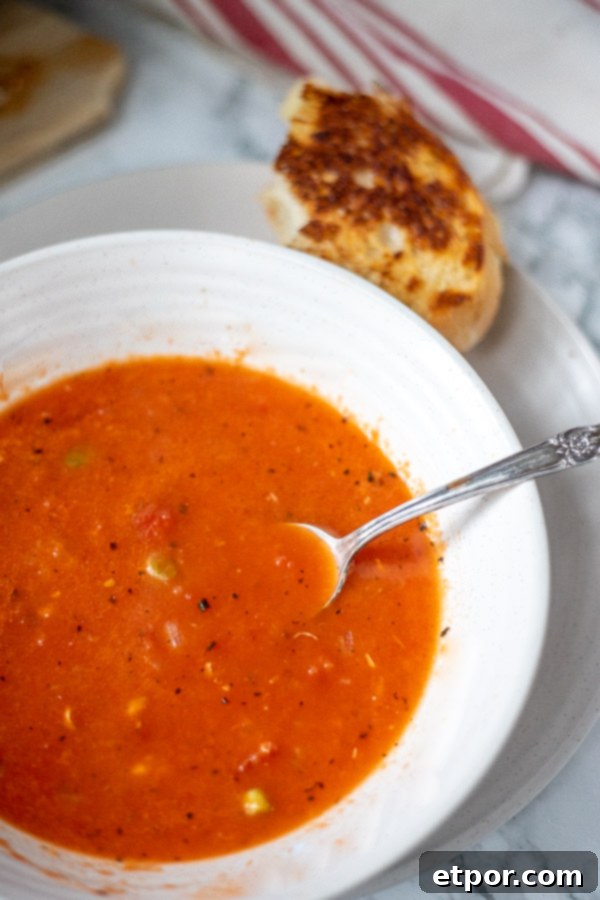 easy tomato soup in a white bowl with grilled cheese on a plate in the background