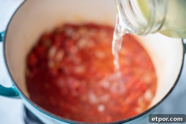 adding broth to tomatoes, onion, and garlic for easy tomato soup