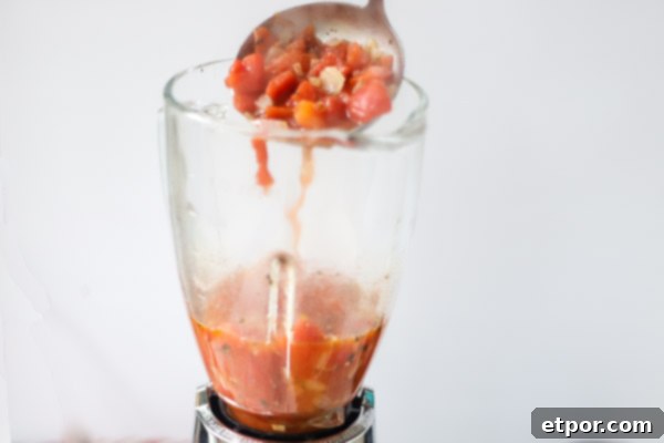 tomato soup being ladled into a blender to puree into tomato soup