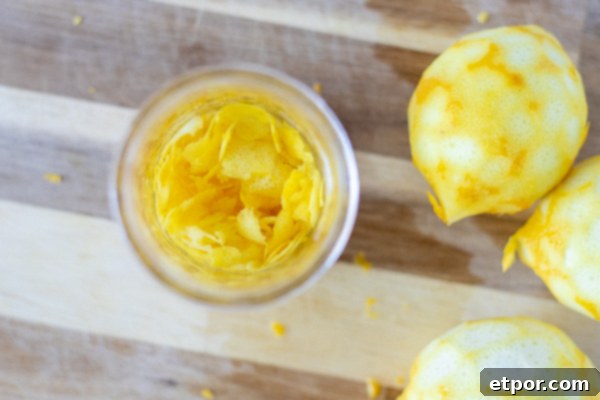 overheard shot of lemon peels in a mason jar with vodka poured over. Lemon are placed to the right