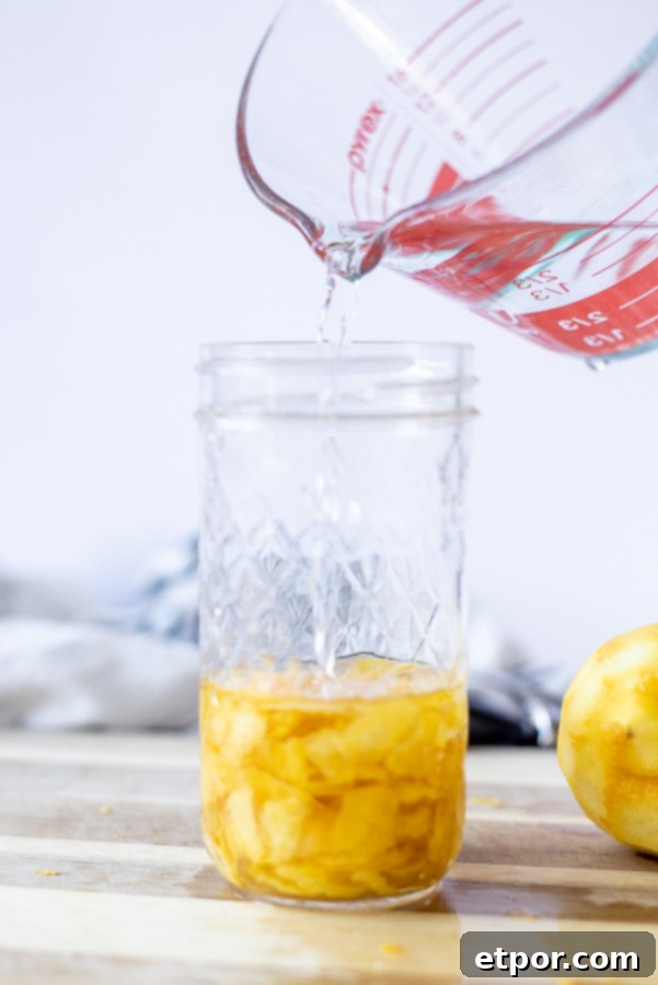 measuring cup of vodka being poured over lemon peels to make homemade lemon extract