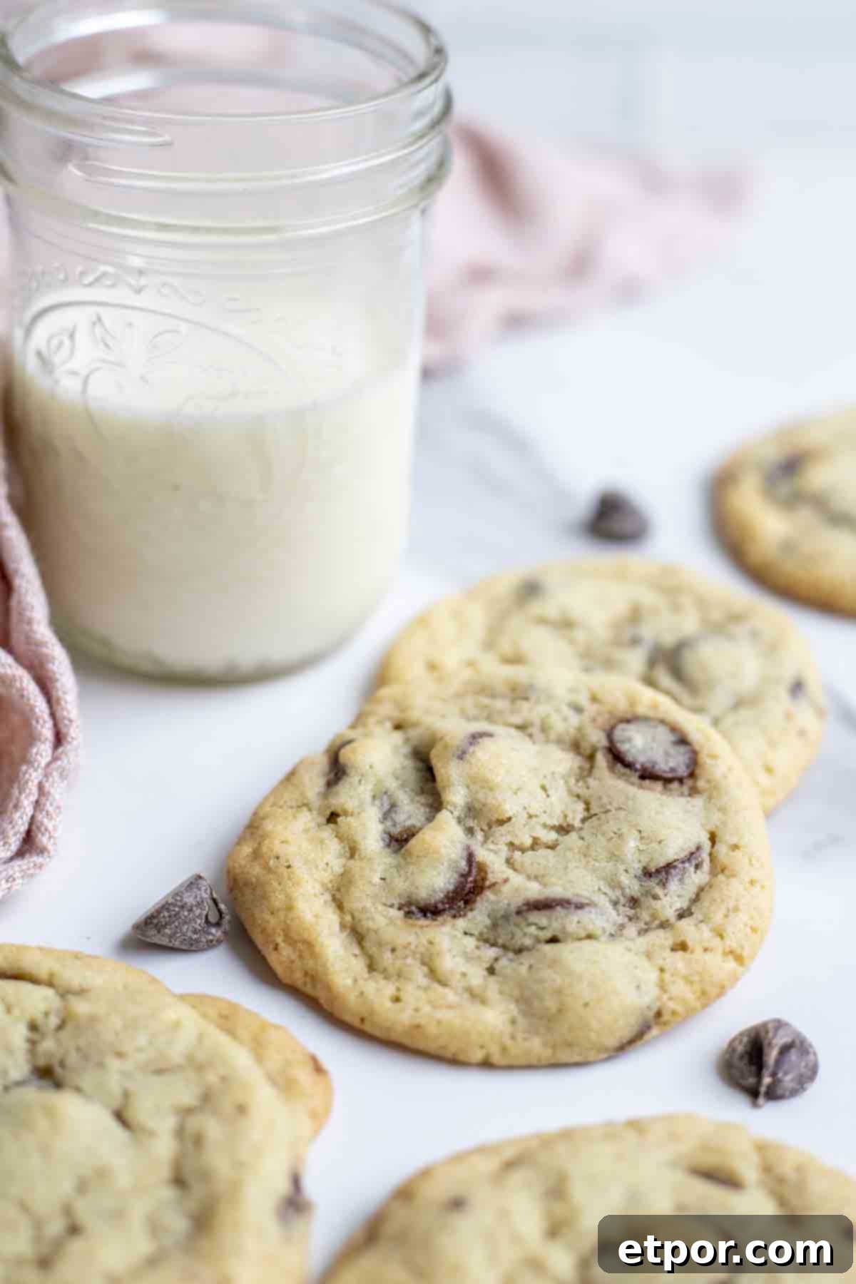 Cultured Chocolate Chip Cookies 2 Soft, chewy sourdough chocolate chip cookies on a marble countertop with a glass of milk and a pink towel in the background, highlighting their delicious texture and golden edges.