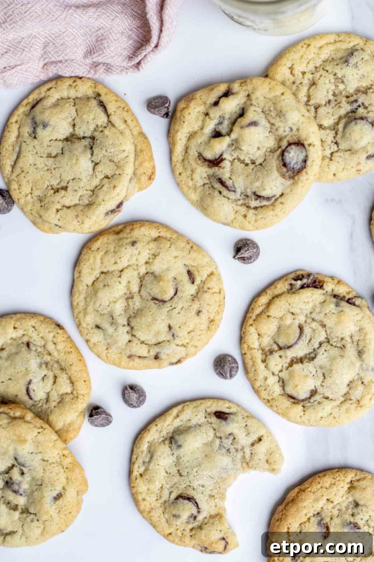 Cultured Chocolate Chip Cookies 11 An overhead photo of perfectly baked sourdough chocolate chip cookies arranged artfully on a countertop. One cookie in the foreground has a bite taken out, revealing its soft, chewy interior and melted chocolate.