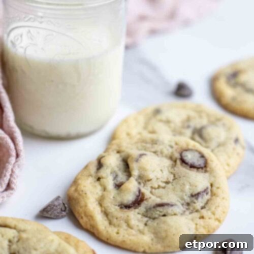 Sourdough chocolate chip cookies on a marble countertop with a glass of milk and a pink towel in the background, showing their delicious appeal.