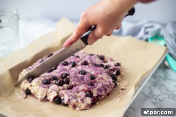 Scone dough being cut into triangular shapes with a knife on parchment paper.