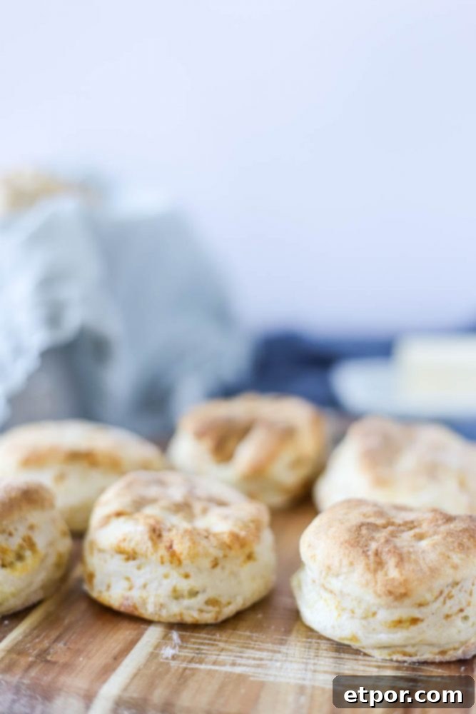sourdough biscuits on a wood cutting board with butter dish and a blue napkin lined bull of biscuits