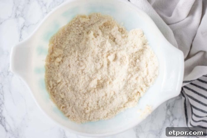 flour and butter combined together in a white bowl with a black and white towel to the right