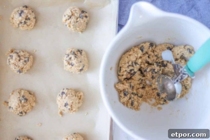 oatmeal chocolate chip cookies being scooped onto a parchment lined baking sheet.