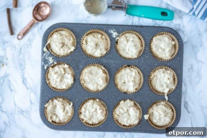 Muffin batter in muffin tins with an ice cream scoop hovering above, ready for baking.
