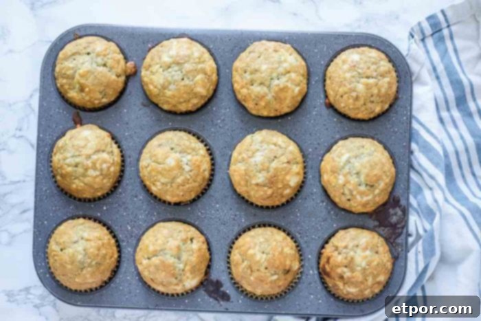 Freshly baked sourdough banana muffins cooling in a muffin tin on a cream and blue striped towel.