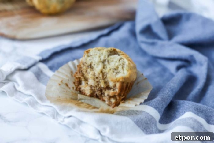 A sourdough banana muffin with a bite taken out, resting on a blue and white towel, showing its tender interior.