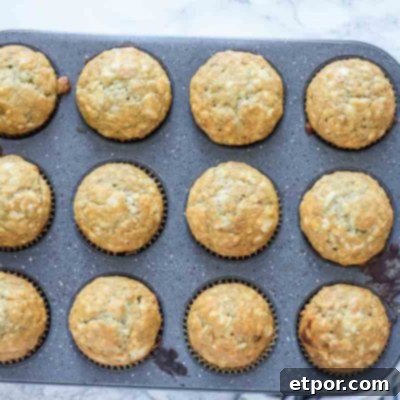 Freshly baked sourdough banana muffins in a muffin tin, on a cream and blue striped towel, ready to be served.
