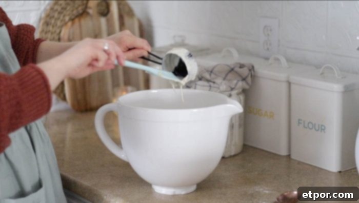 Adding sourdough starter to a stand mixer bowl with other ingredients for the muffin batter.