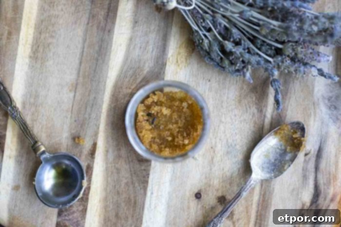 Whip Up Your Own Lip Scrub 11 overhead photo of lip scrub in a glass jar with a measuring spoon and a tea spoon around the jar. A bundle of lavender is in the background