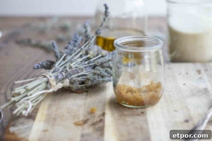 Whip Up Your Own Lip Scrub 6 jar of brown sugar lip scrub on a wood cutting board with dried lavender and two jars of sugar and oil in the background
