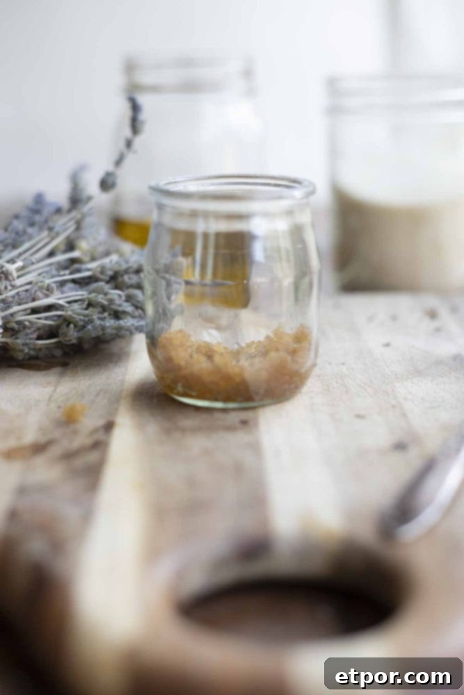 Whip Up Your Own Lip Scrub 7 jar of brown sugar lip scrub on a wooden cutting board with a bundle of lavender and jars of oil and sugar in the background