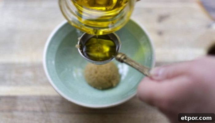Whip Up Your Own Lip Scrub 8 oil being added to brown sugar in a teal bowl