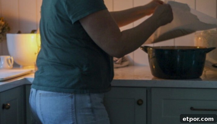Placing sourdough bread dough on parchment paper into a cold Dutch oven.