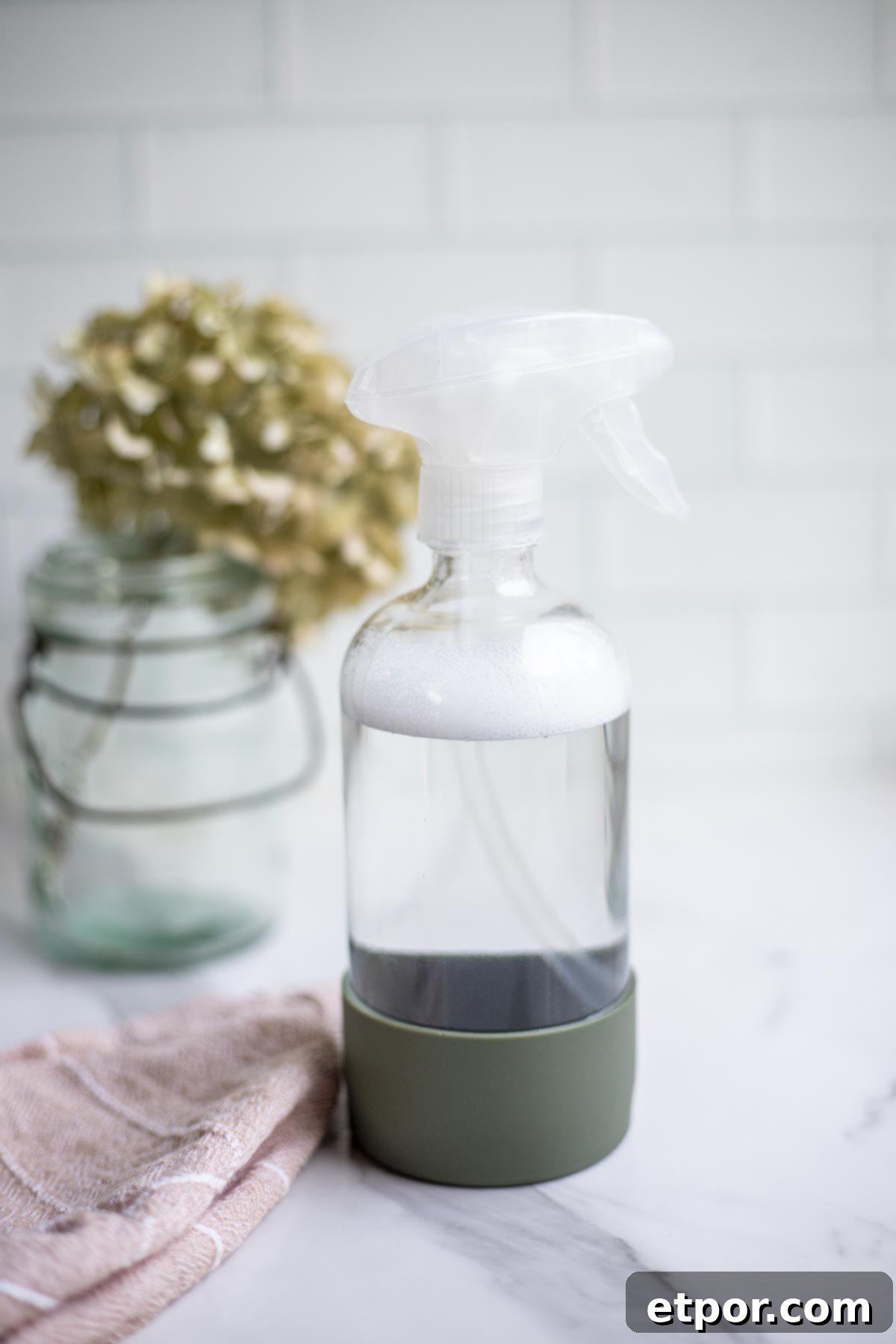 homemade granite cleaner in a spray bottle with a pink towel and a dried flowers in the background.