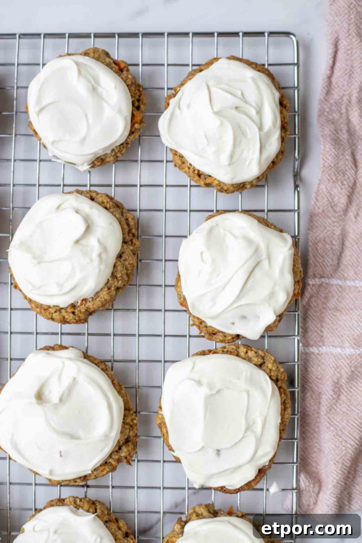 overhead photo of sourdough carrot cake cookies topped with whipped cream frosting on a cooling rack.