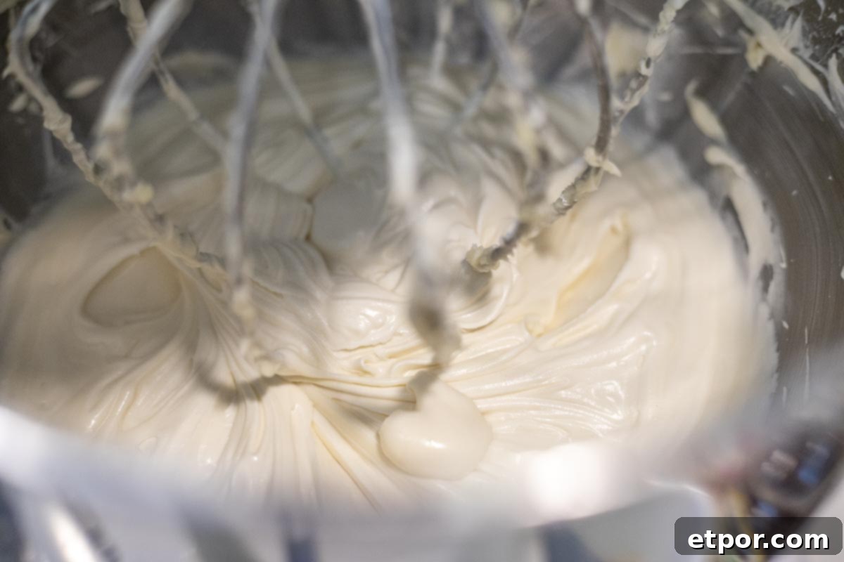Cream cheese frosting whipped in a stand mixer bowl with balloon whisk.