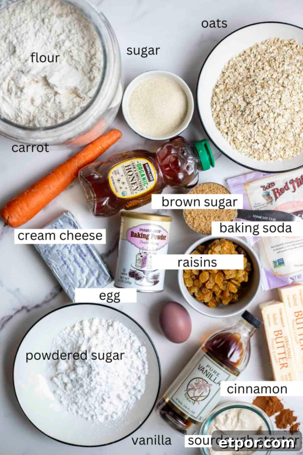 Oats, flour, raisins, carrot, eggs, and other ingredients on a marble countertop.