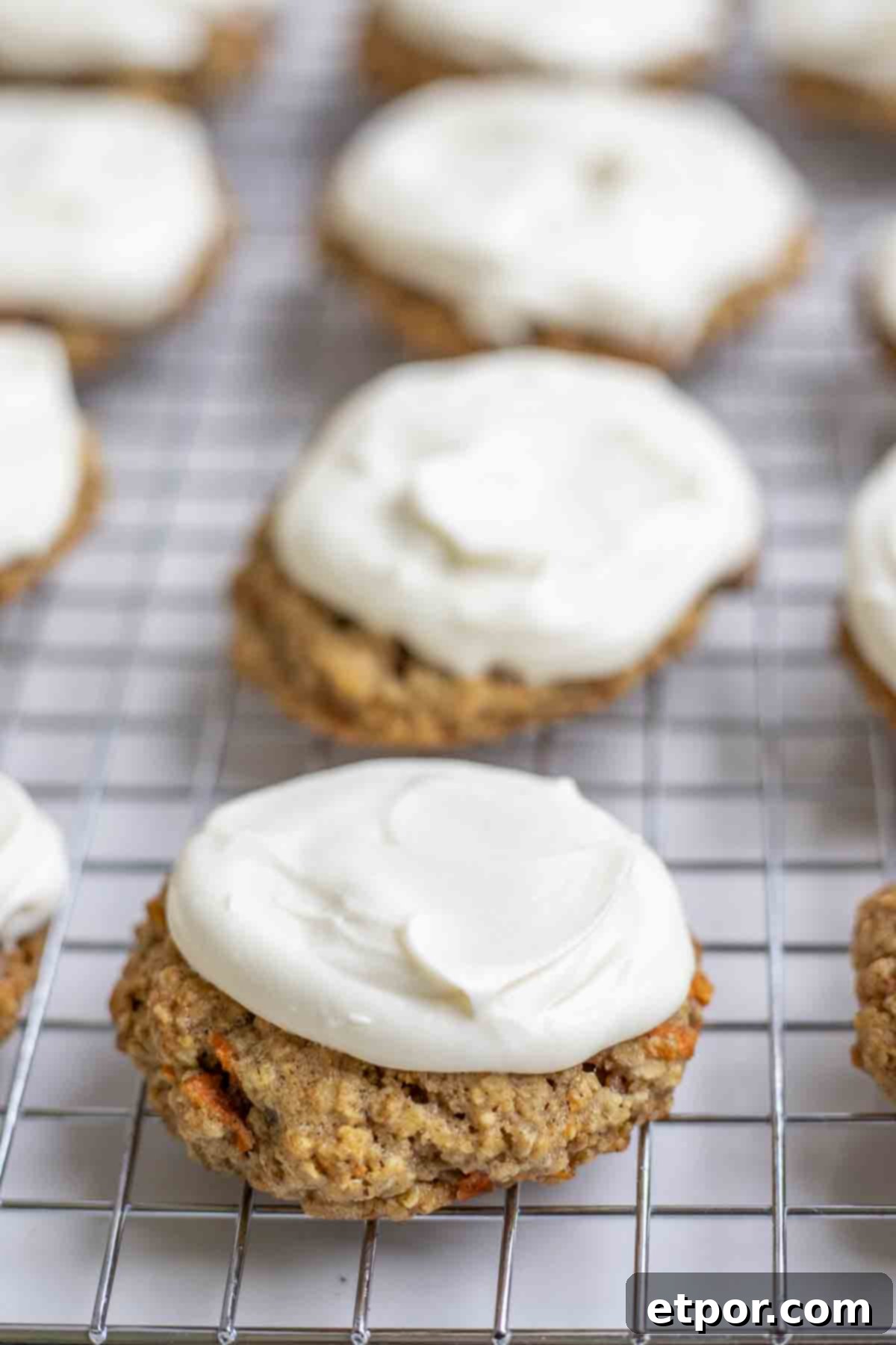 Sourdough carrot cake cookies topped with cream cheese frosting on a wire rack.