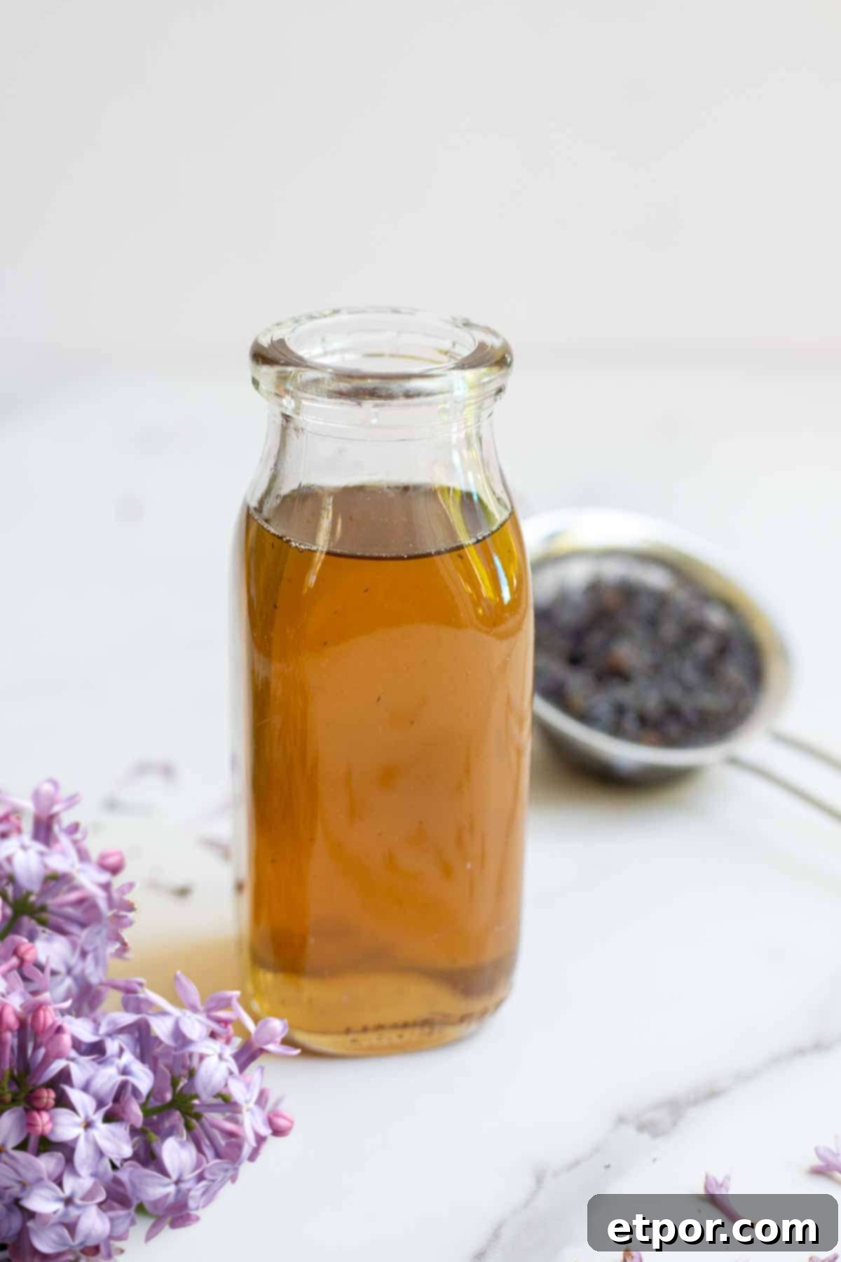 Lilac syrup in a bottle with strained flowers in the background and fresh flowers in the front.