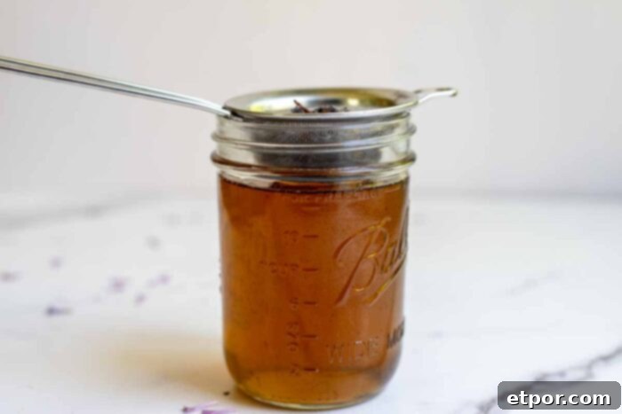 Straining lilac syrup into a mason jar on a countertop.