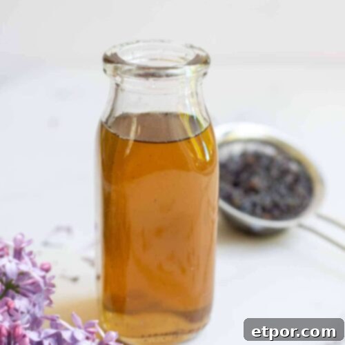 Lilac syrup in a bottle with strained flowers in the background and fresh flowers in the front.
