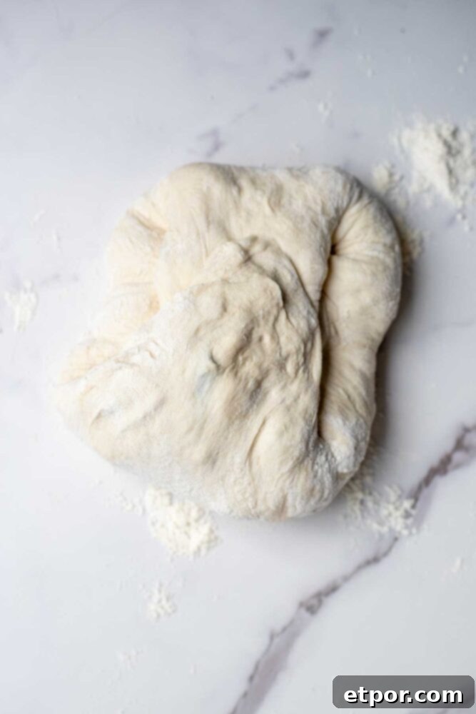 Folding sourdough blueberry cream cheese dough up and into the center on a countertop.