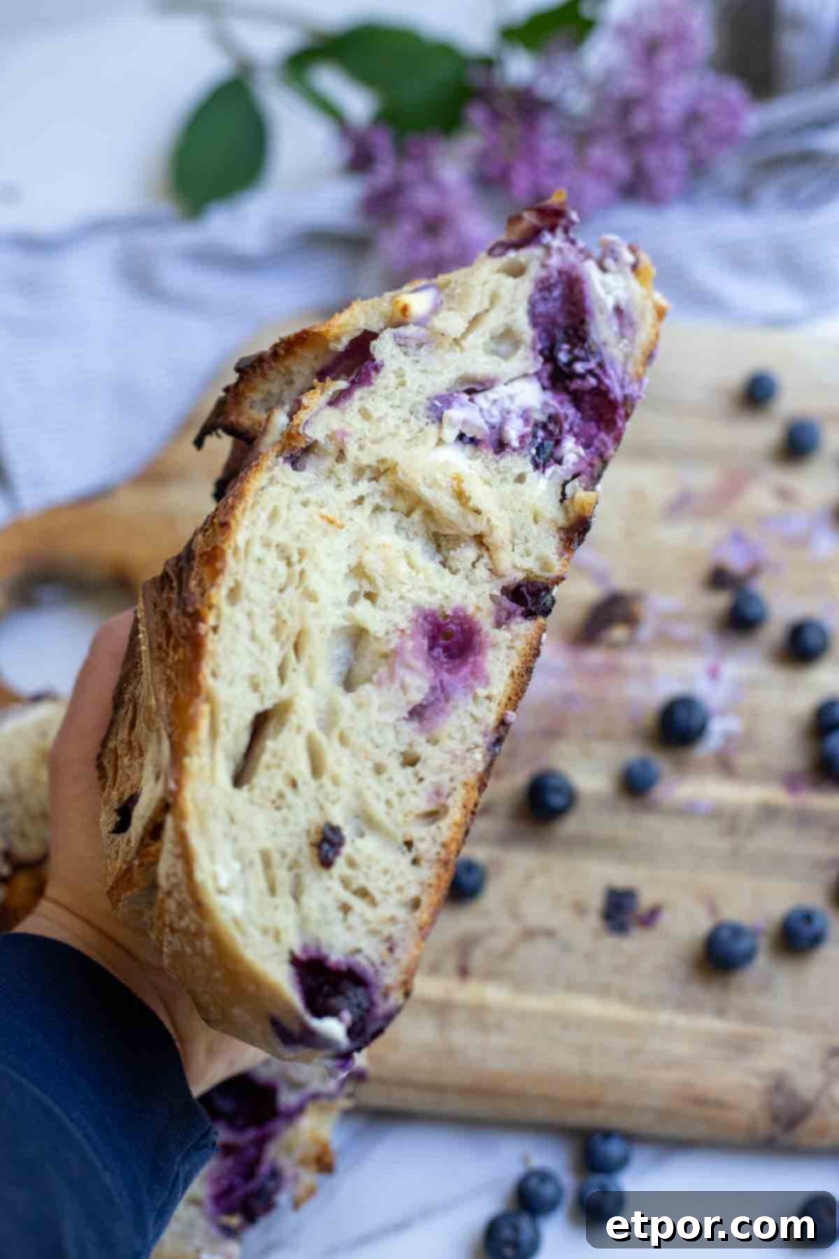Hand holding a half of a loaf of sourdough blueberry bread.