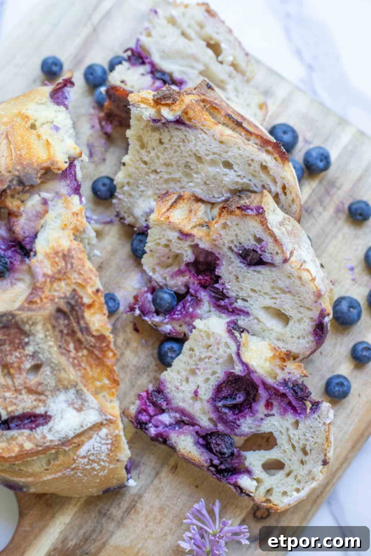 Sourdough blueberry cream cheese boule sliced on a wooden cutting board with fresh blueberries scattered.