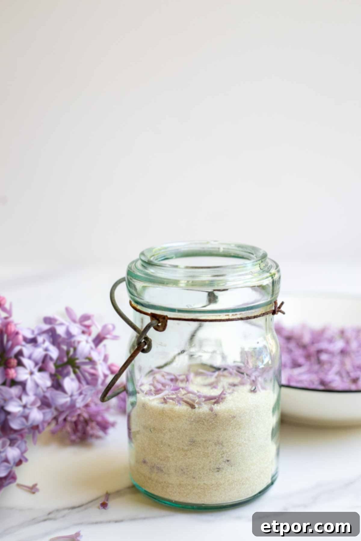 Lilac sugar in an antique mason jar with fresh lilac in the background.