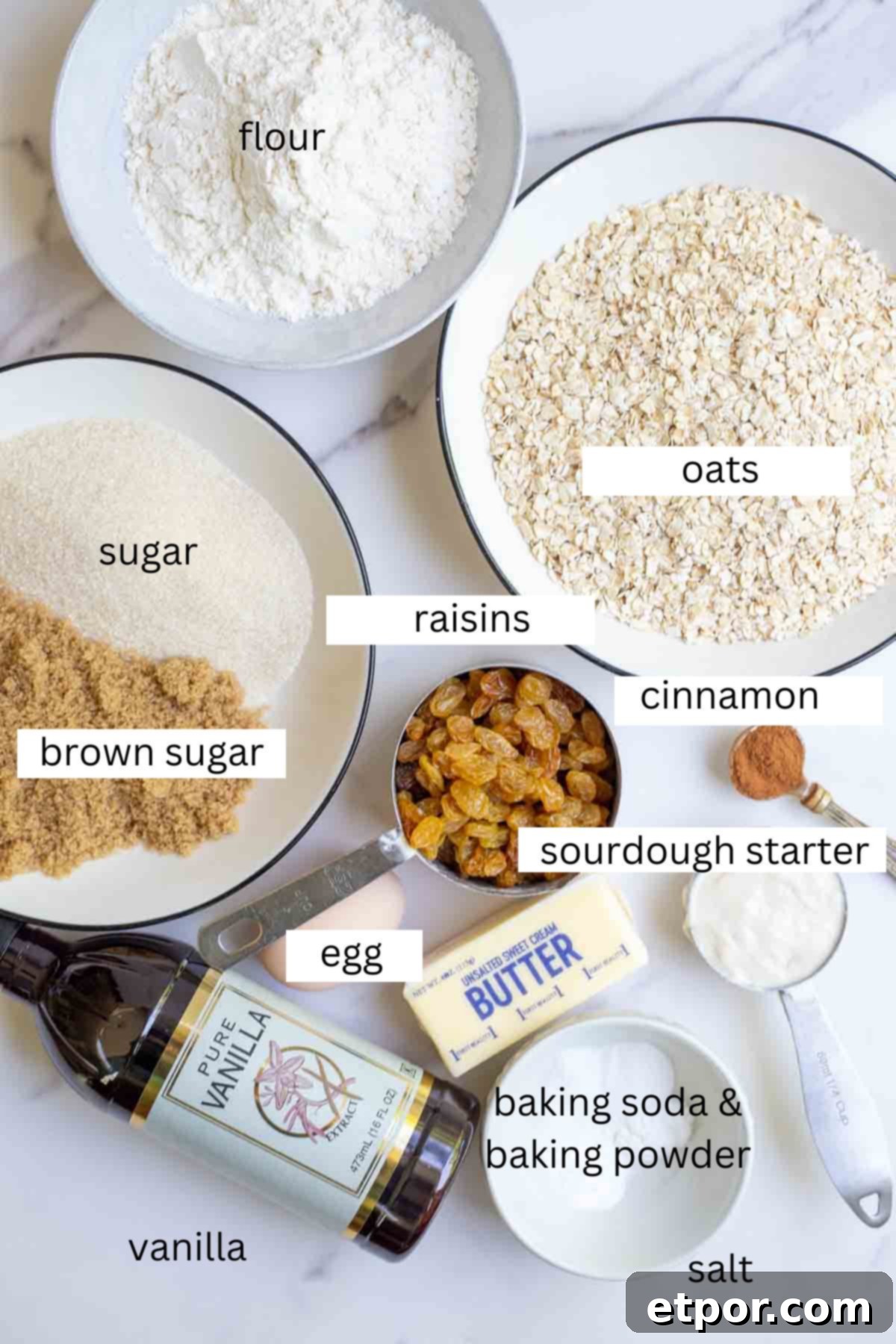Various baking ingredients laid out: bowls of oats, all-purpose flour, brown sugar, and regular granulated sugar, surrounded by eggs, butter, vanilla extract, and sourdough discard.