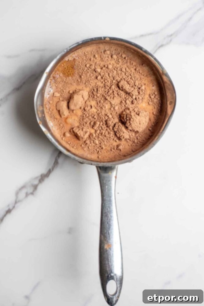 Milk, cocoa powder, maple syrup, pumpkin puree, pumpkin spice and other ingredients in a saucepan.