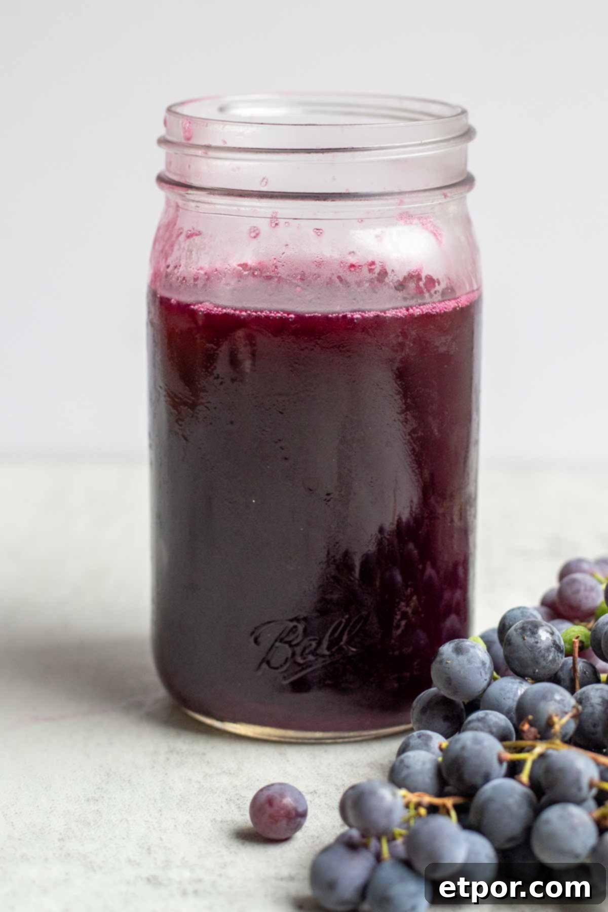 Close up picture of homemade grape juice in a quart mason jar with grapes in front.