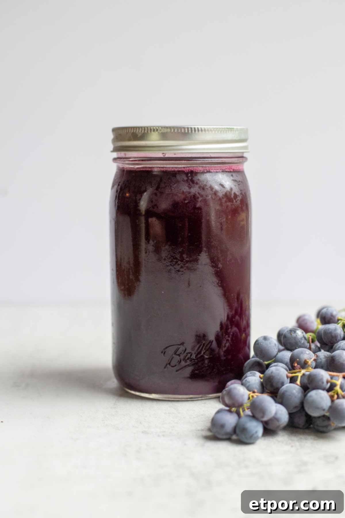 Canned grape juice in a quart jar with grapes in front of the jar.