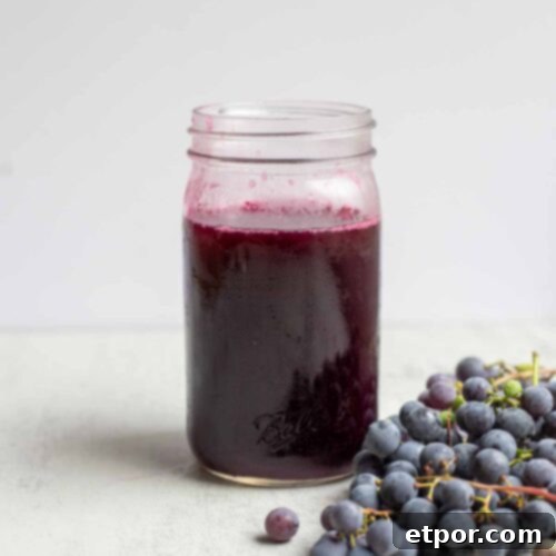 jar of homemade grape juice with a bunch of grapes in front of the jar.