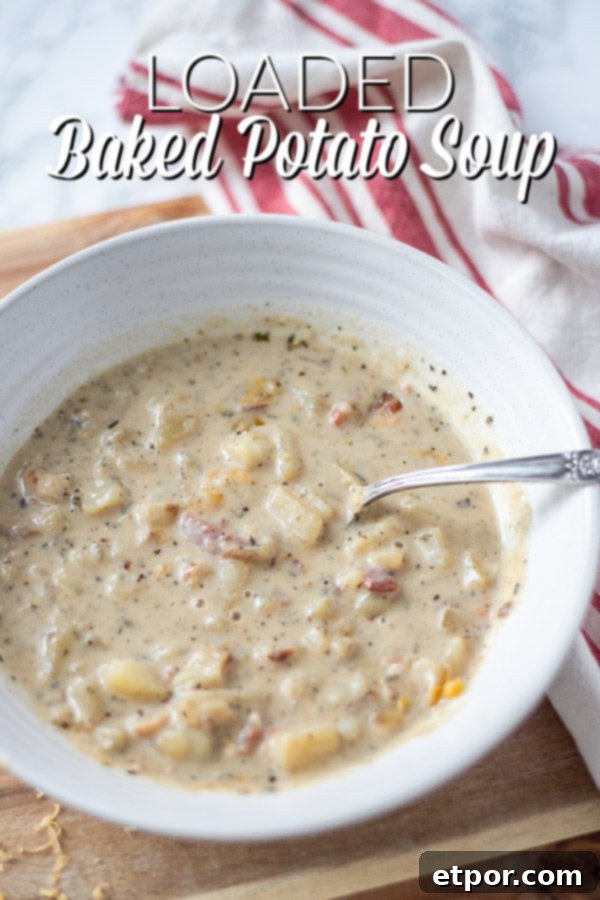 bowl of baked potato soup with bacon on a wood cutting board with a red and cream napkin to the right.