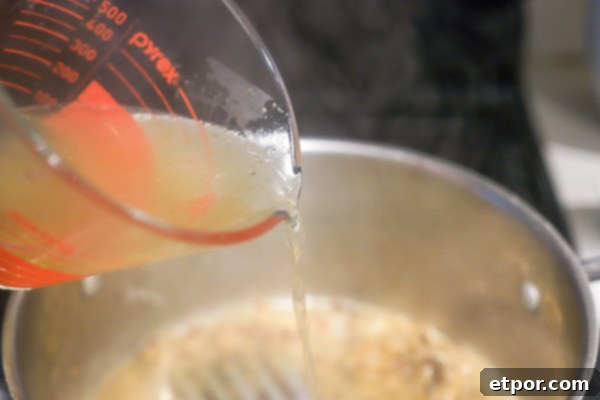 chicken broth being slowly poured into pot with onions ad flour