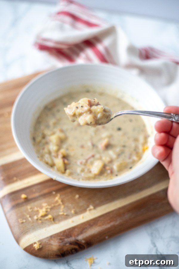 spoonful of potato bacon soup over a bowl on a wooden cutting board