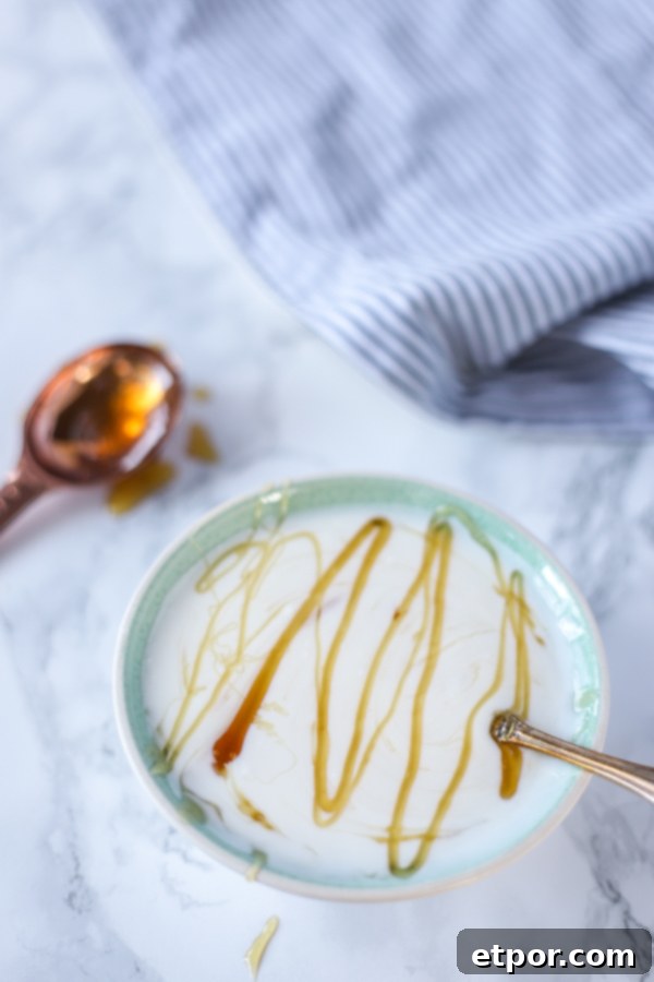 A bowl of creamy homemade yogurt drizzled with golden honey, with a copper spoon holding more honey in the background, highlighting natural sweetness.