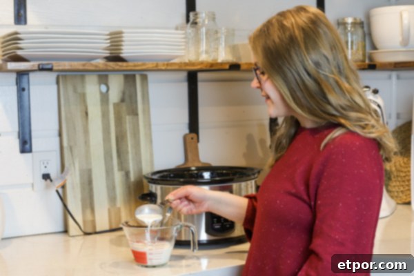 Woman adding yogurt starter to milk in a Pyrex measuring cup for homemade yogurt, demonstrating an essential step in the process.
