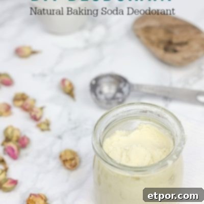 Homemade DIY deodorant in a clear glass jar, placed on a white washcloth with scattered rosebuds and a stainless steel measuring spoon nearby.