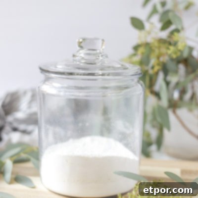 homemade laundry detergent in a glass dish with a lid on a wood cutting board with a mason jar full of eucalyptus