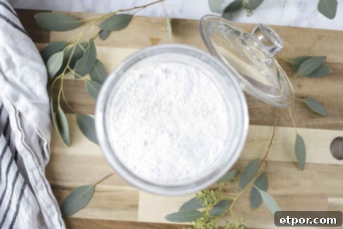 overhead photo of homemade laundry detergent in a glass jar on a wood cutting board with eucalyptus leaves spread around.